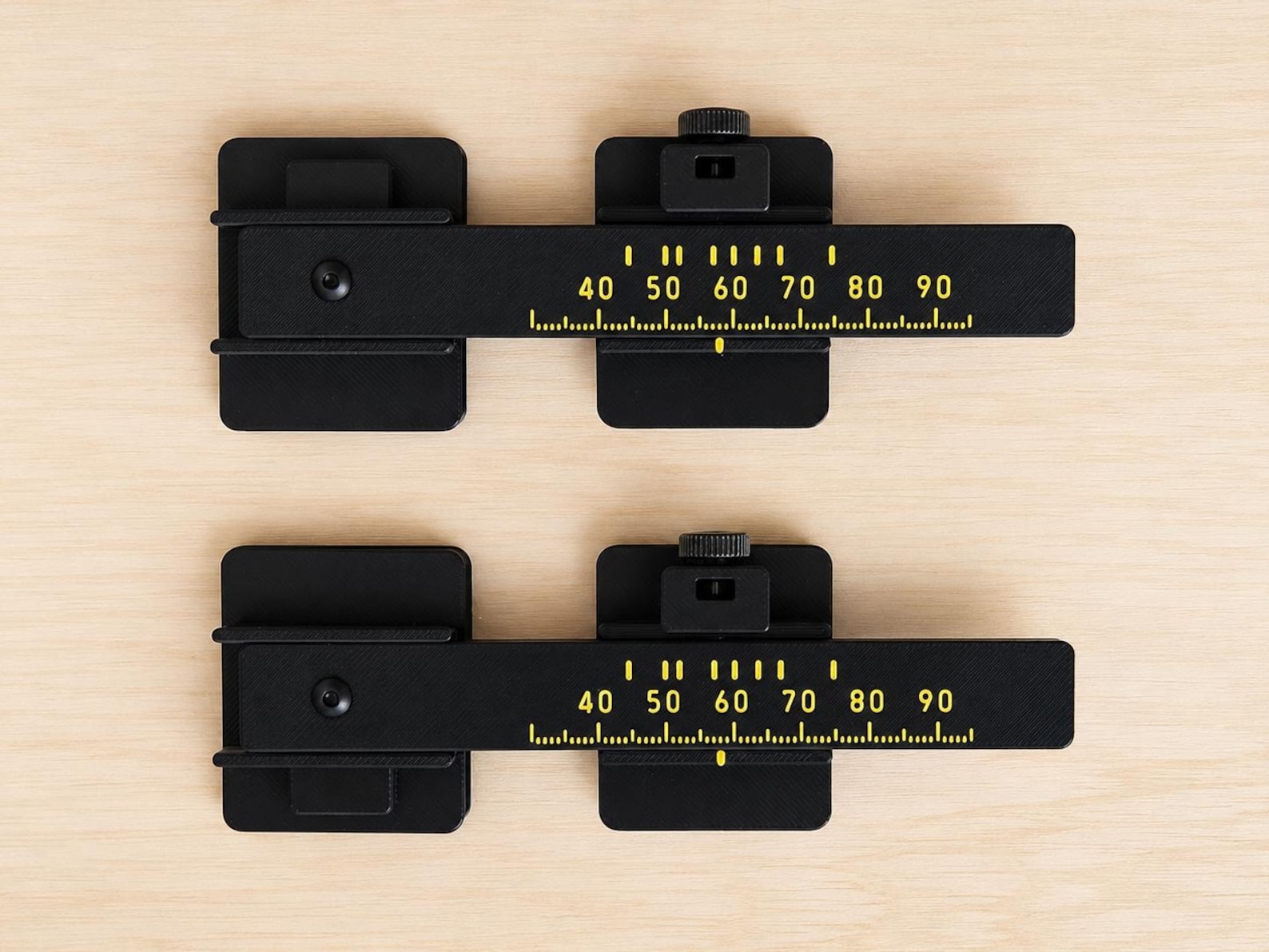 Two black adjustable model railroad track-spacing tools with raised yellow measurement markings